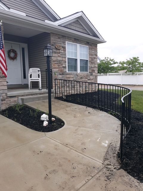 Front porch with wheelchair ramp, black railings, stone house exterior, and a white chair by the door