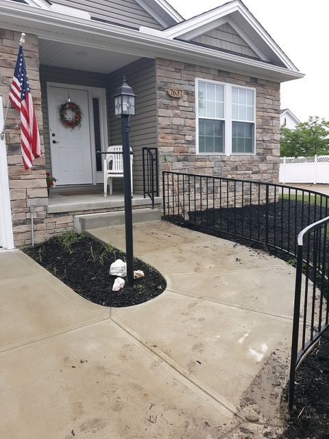 Front porch with concrete ramp and black railing leading to a house entrance, with an American flag and wreath.