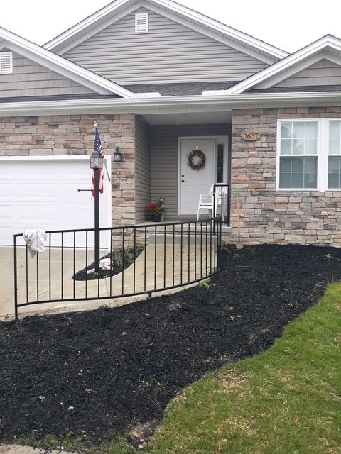 Front porch of a brick house with black railing, stone steps, and a wheelchair ramp leading to the entry.