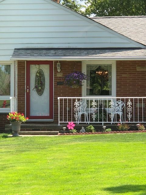 Front porch of a brick house with a white door, hanging flowers, and a green lawn.