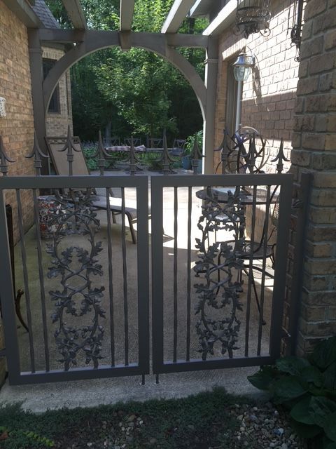 Black wrought-iron gate in a brick courtyard entrance with an arched stone walkway behind it.