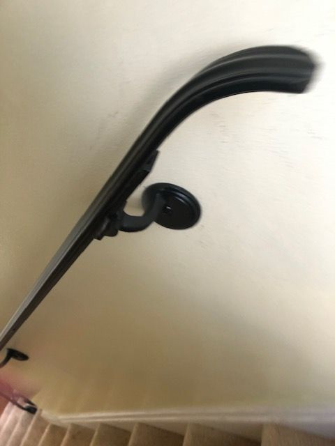 Black metal stair railing with a curved handrail mounted on a beige wall and ceiling.