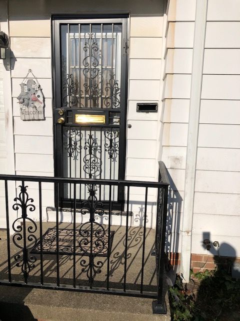 Front porch with black wrought-iron gate, white house facade, and decorative doormat by the door.
