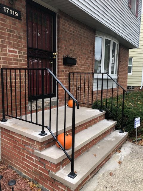 Brick row house front steps with black railings and two orange pumpkins on the stairs