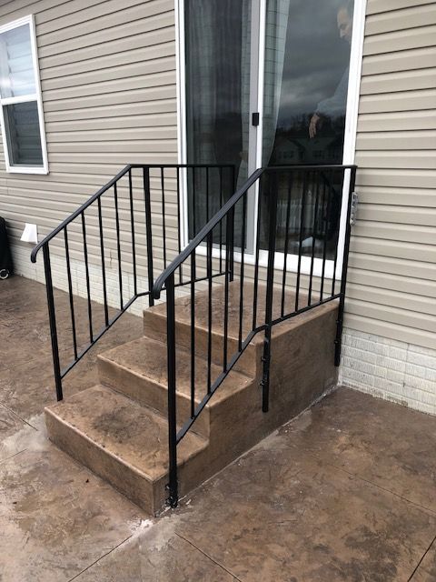 Small concrete steps with black metal handrails leading to a glass door on a beige house.