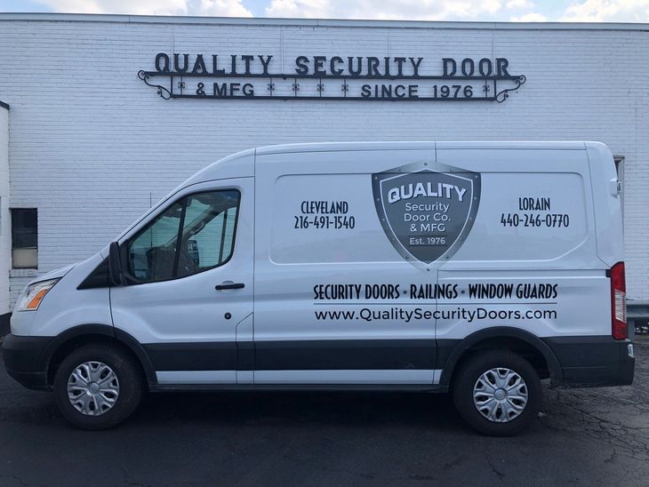 A white work van parked in front of a building with Quality Security Door & Mfg signage. A white work van parked in front of a building with Quality Security Door & Mfg signage.