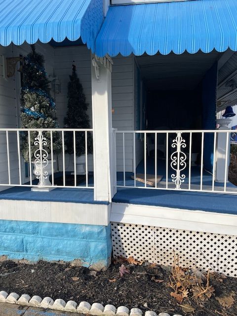 Blue-awning porch with white railing and columns, blue trim, and potted greenery behind the entrance.