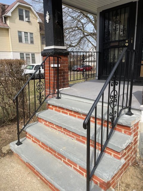Front porch steps with brick and concrete, black metal railings, and a house entrance.