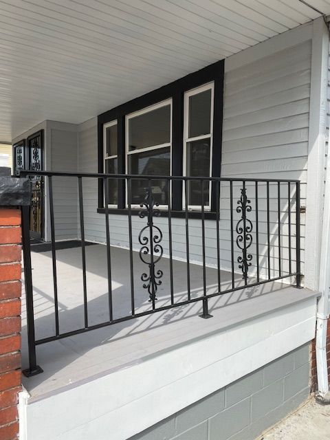 Front porch with black railings, gray siding, and double front doors under a covered roof.