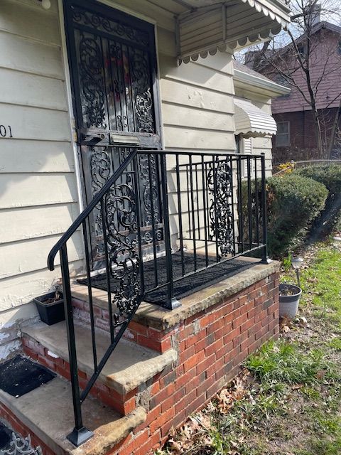 Front porch steps with black metal railing and brick base on a house exterior