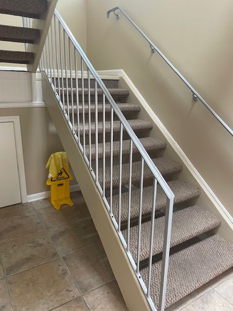 Carpeted indoor staircase with white railings and a yellow wet floor sign at the bottom.