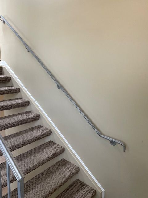 Carpeted stairwell with a silver handrail along a beige wall.
