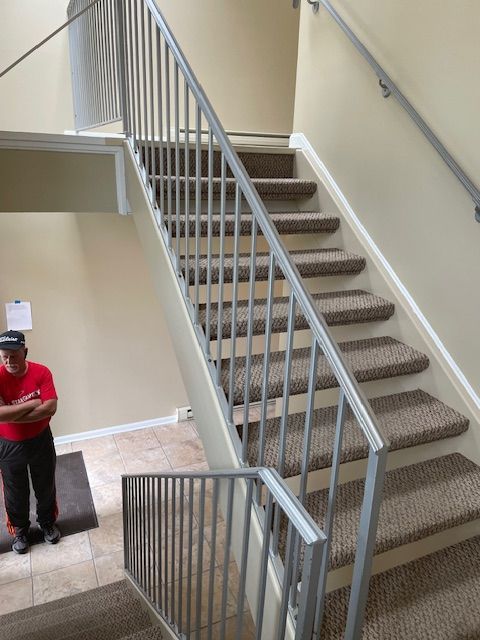 Indoor stairwell with carpeted steps and white railings; a person stands at the lower left near a doorway.