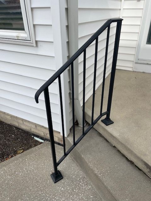 Black metal handrail beside concrete steps and a house wall