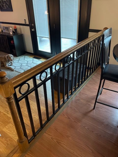 Indoor staircase railing with black metal balusters and wood handrail beside a hallway and entry door