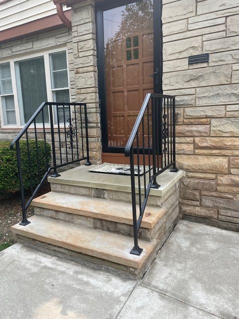 Front steps and wooden door of a stone house with black metal railings and concrete walkway