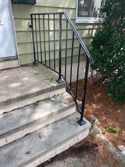 Black metal handrail beside concrete steps leading to a building entrance.