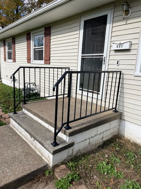 Small front porch with black railing, concrete steps, screen door, and house number 87 on a light-sided home.