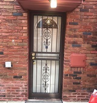 Brick house front door with black wrought-iron screen and red brick wall