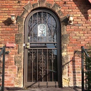Brick building doorway with arched black wrought-iron gate and sunlit stone trim