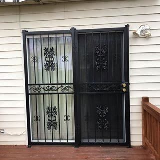 Black metal security door on a white house exterior beside a wooden deck railing