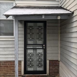 Front entry door with decorative black metal screen beneath a small awning and porch roof.