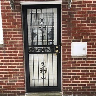 Black metal security door with frosted glass in a red brick wall.
