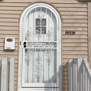 White security door with ornate bars, mailbox, and house number 19519 on beige siding