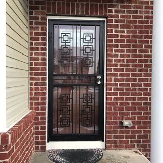Black metal security door with geometric glass panels set in a red brick entryway