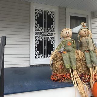 Fall porch display with two scarecrow dolls on hay bales beside a white front door