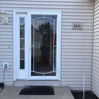 Front entrance with white door, sidelight windows, black mat, and house number 2031 on beige siding