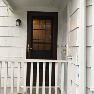 White porch with dark front door, black lamp, and railing.