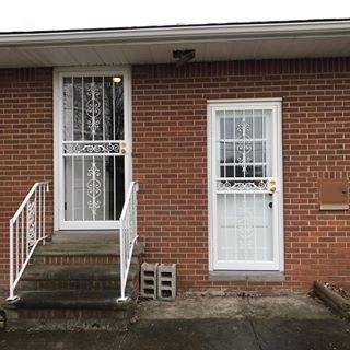 Brick house front entrance with two white security doors, small steps, and a metal railing.