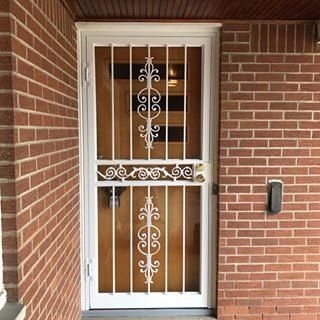 White wrought-iron security door set in a brick entryway with a small wall-mounted keypad