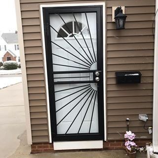 Black security door with frosted glass on a house exterior, beside a mailbox and wall lantern.
