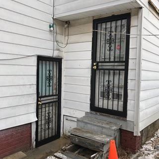 Side entrance to a white house with two black security doors and concrete steps.