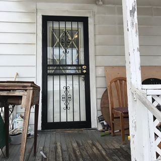 Front porch with a black security door, weathered wood floor, chair, and small table.