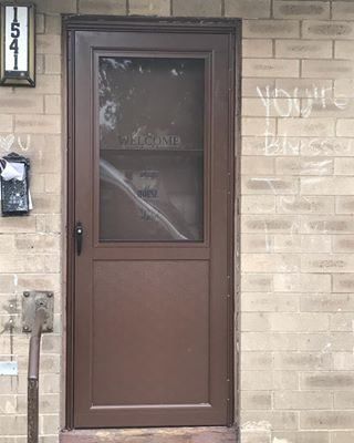 Brown front door with a screen, house number 154, and graffiti on the brick wall beside it