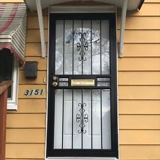 Black security door with barred windows and house number 3151 on a yellow exterior wall