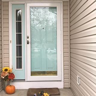 Front porch with a light blue door, white trim, pumpkins, and fall flowers by the entrance.
