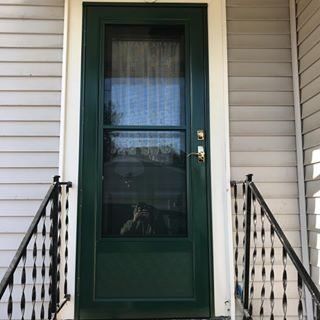 Green front door with sidelights and black railings on a house porch
