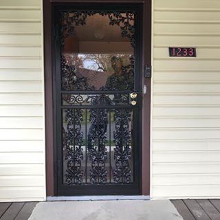 Black iron front door with glass panel, side light, and house number 1233 on beige siding.