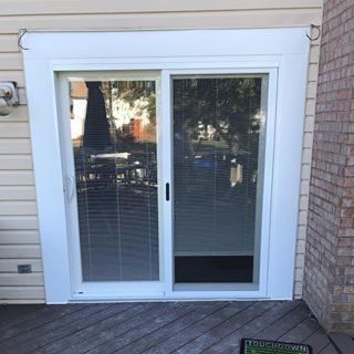 White sliding glass patio door with blinds, beside siding and brick wall on a deck