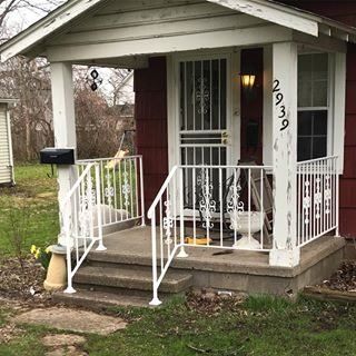 Small front porch with white railings, dark red door, and house number 2939 on a gray house