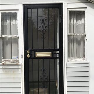 Black security door between two white-trimmed windows on a house exterior