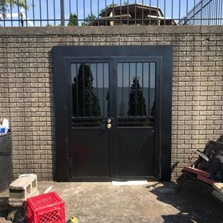 Black double metal gate set in a stone wall with a concrete walkway in front