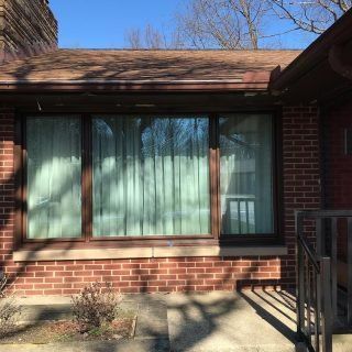 Brick house front window with green curtains and a small porch railing in sunlight