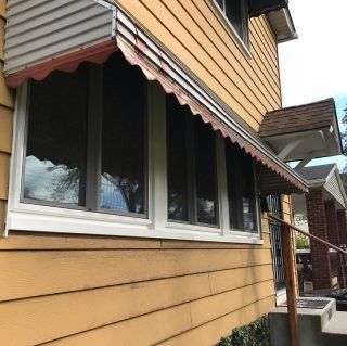 Yellow house exterior with dark awnings and a row of windows under a sloped roof