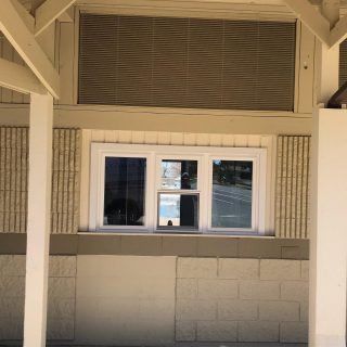 Covered porch with white columns, tan walls, and a central window under a louvered vent.