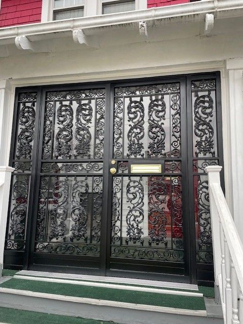 Black ornate metal double gate with glass panels at a building entrance, framed by white columns and steps